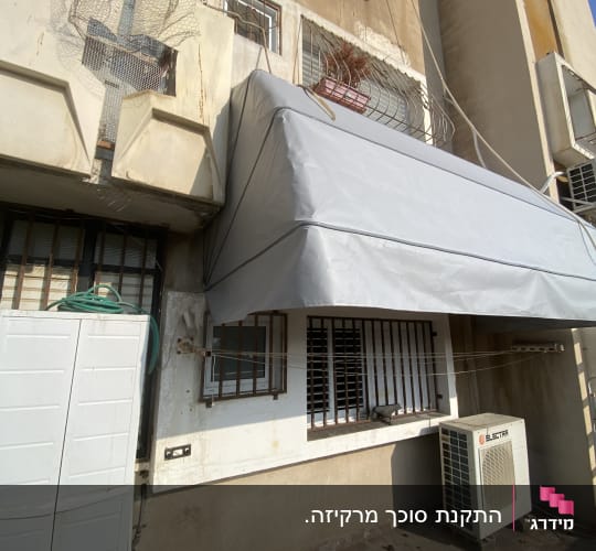 סוכך מרקיזה מתקפל בכיסוי אפור מותקן מעל חלונות בחזית מבנה